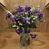 Bouquet of purple and white flowers in a clear vase on a wooden surface