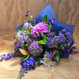 Bouquet of purple, blue and pink flowers with blue paper on a wooden surface
