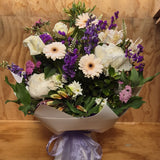 Bouquet of flowers with white, purple, and green colours presented in a water box.