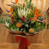 Bouquet of tropical flowers with green leaves and orange accents on a wooden surface.
