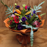 Colourful bouquet of flowers wrapped in brown paper with an orange ribbon on a wooden surface.