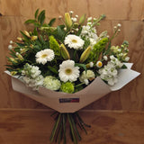 A bouquet of flowers featuring white and green colors, wrapped in white paper . The bouquet includes various flowers such as lilies, gerbera daisies, and other greenery.