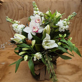 A bouquet presented in a water box. It consists of two white orchids, white lilies, alstroemaria and stock. It has a natural hessian wrap and bow.