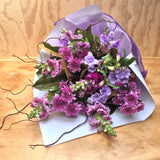 A bouquet of mauve chrysanthemums, snap dragons and lilac freesias, wrapped in white kraft paper.