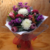 Bouquet of white, purple and reddish pink flowers wrapped in white paper with a red ribbon on a wooden surface