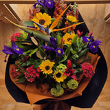 Colourful bouquet of flowers with a mix of sunflowers, purple iris, and red flowers wrapped in orange and black craft paper