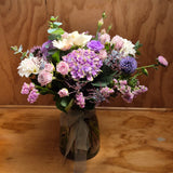 Bouquet of hydrangea, mini roses, dahlia, gerberas, lisianthus, statice and foliage presented in a glass vase.