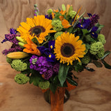 Bouquet of sunflowers, purple iris, orange lilies and birds of paradise and greenery presented in a glass vase