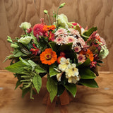 Orange, cream, apricot and green flowers and foliage in a vase.