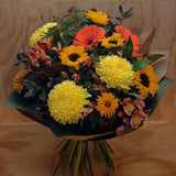 Bouquet of colourful flowers including yellow, and orange, flowers on a wooden surface.