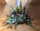 Arrangement of flowers and foliage in a landscape style, on a wooden surface.