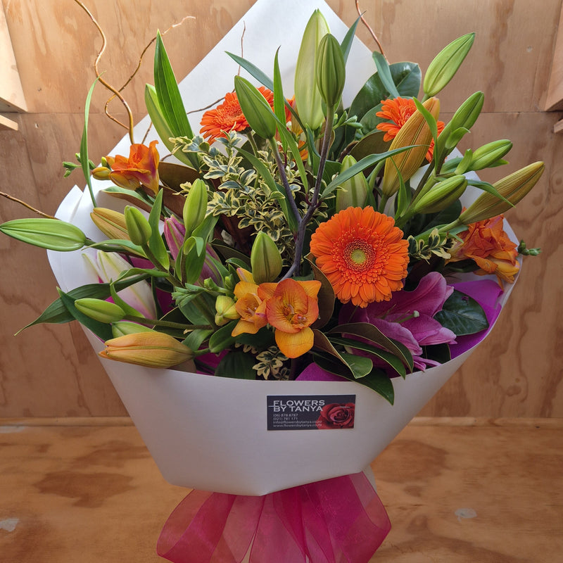 A bouquet wrapped in white paper, orange, white and  pink flowers, with foliage.