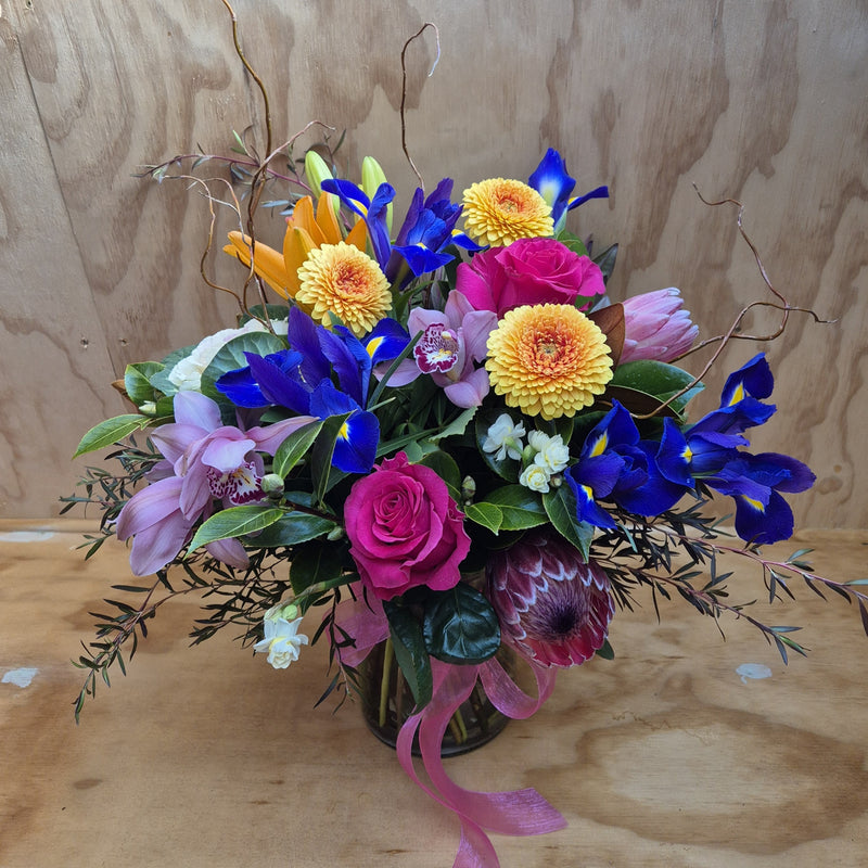 Colorful flower arrangement with pink, yellow, and blue flowers in a vase.