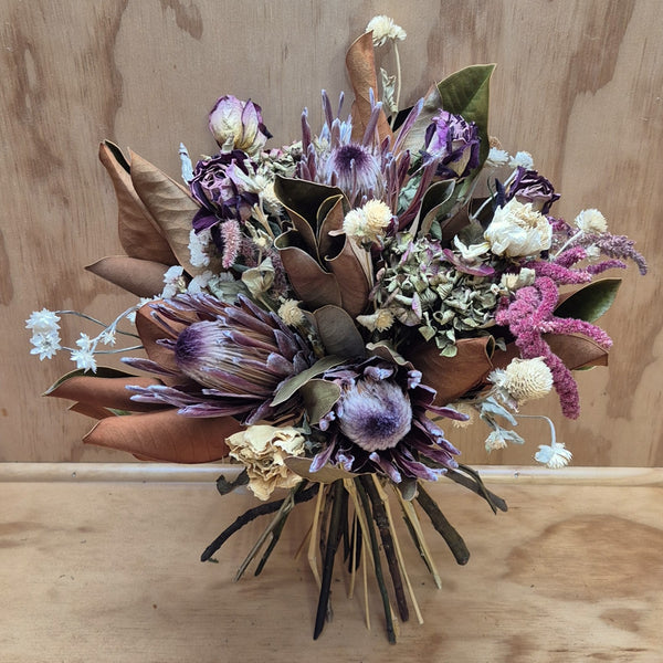 Bouquet of dried flowers with purple, brown, and green tones on a wooden surface.