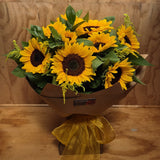 Bouquet of sunflowers in a cardboard box with yellow ribbon on a wooden surface.