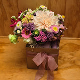 A gift box with a soap bar and hand cream, and a vase of pretty pink flowers.