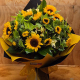 Bouquet of sunflowers wrapped in yellow and black paper with a yellow bow.