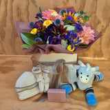 a box to welcome a baby containing flowers, a giraffe soft toy, hand knitted bootees and hat, and a hand cream and soap