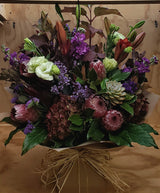 Bouquet of autumn hydrangeas, protea , white lisianthus and purple flowers with a brown paper wrap in a water box.