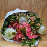 Bouquet of pink and white tropical  flowers wrapped in white paper on a wooden surface