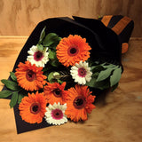 Bouquet of orange, white and pink gerberas wrapped in black paper on a wooden surface.
