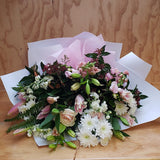 Lilies, chrysanthemums, tock and freesias make up a bouquet. It is wrapped in white craft paper