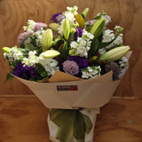 Bouquet of purple and white flowers wrapped in kraft paper and in a water box.