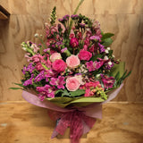 Bouquet of mixed pink flowers with green leaves presented in a water box .