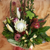Bouquet of long lasting flowers and lush greenery including a king protea, protea pink ice and lilies on a wooden surface