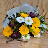 Bouquet of yellow, white and burgundy gerberas with  on a wooden surface.