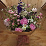 A floral arrangement featuring a variety of wild garden flowers including pink, white, and purple flowers, with green leaves and stems, arranged in a cardboard vase.