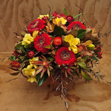 Vase of red, yellow, and green flowers on a wooden surface