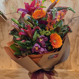 Bouquet of rich autumn toned flowers wrapped in brown and orange paper.