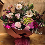 Bouquet of flowers with pink and burgundy tones presented in a water box, wrapped in pink craft paper